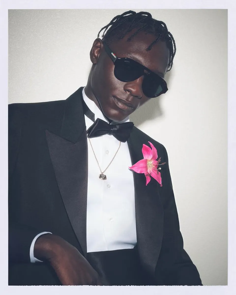 Gucci eyewear campaign, Spring-Summer 2026: a young man in a tuxedo with a bow tie and a pink flower in his lapel, wearing black sunglasses