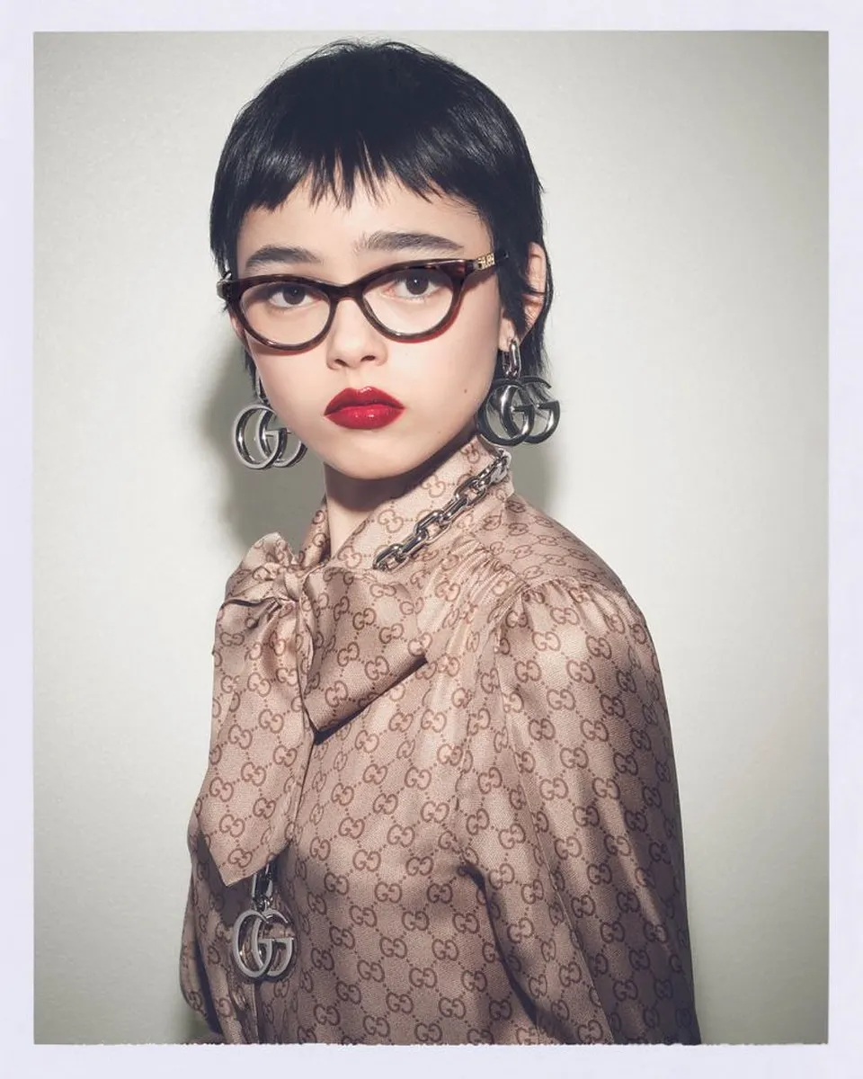 Gucci eyewear campaign, Spring-Summer 2026: a woman with short black hair in a GG-print blouse, wearing havana cat-eye optical glasses