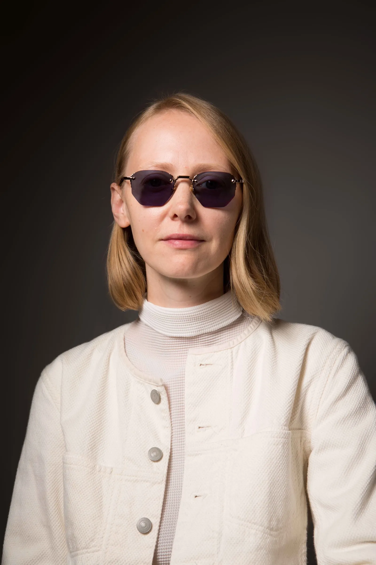 A woman in a white jacket wearing Massada Pentagon Essential sunglasses with dark lenses