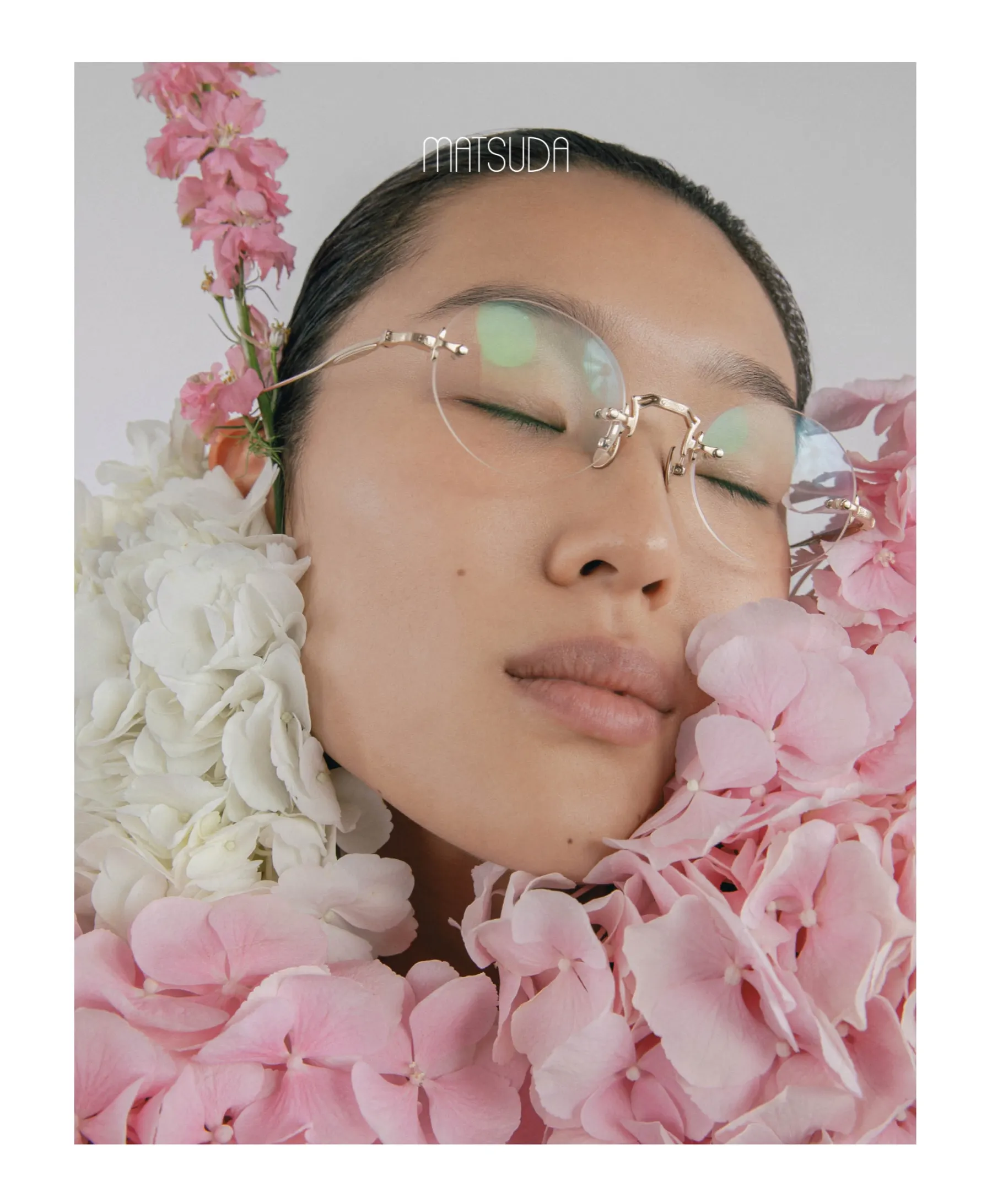 A woman wearing Matsuda M5002 optical glasses in Brushed Gold, surrounded by pink hydrangeas