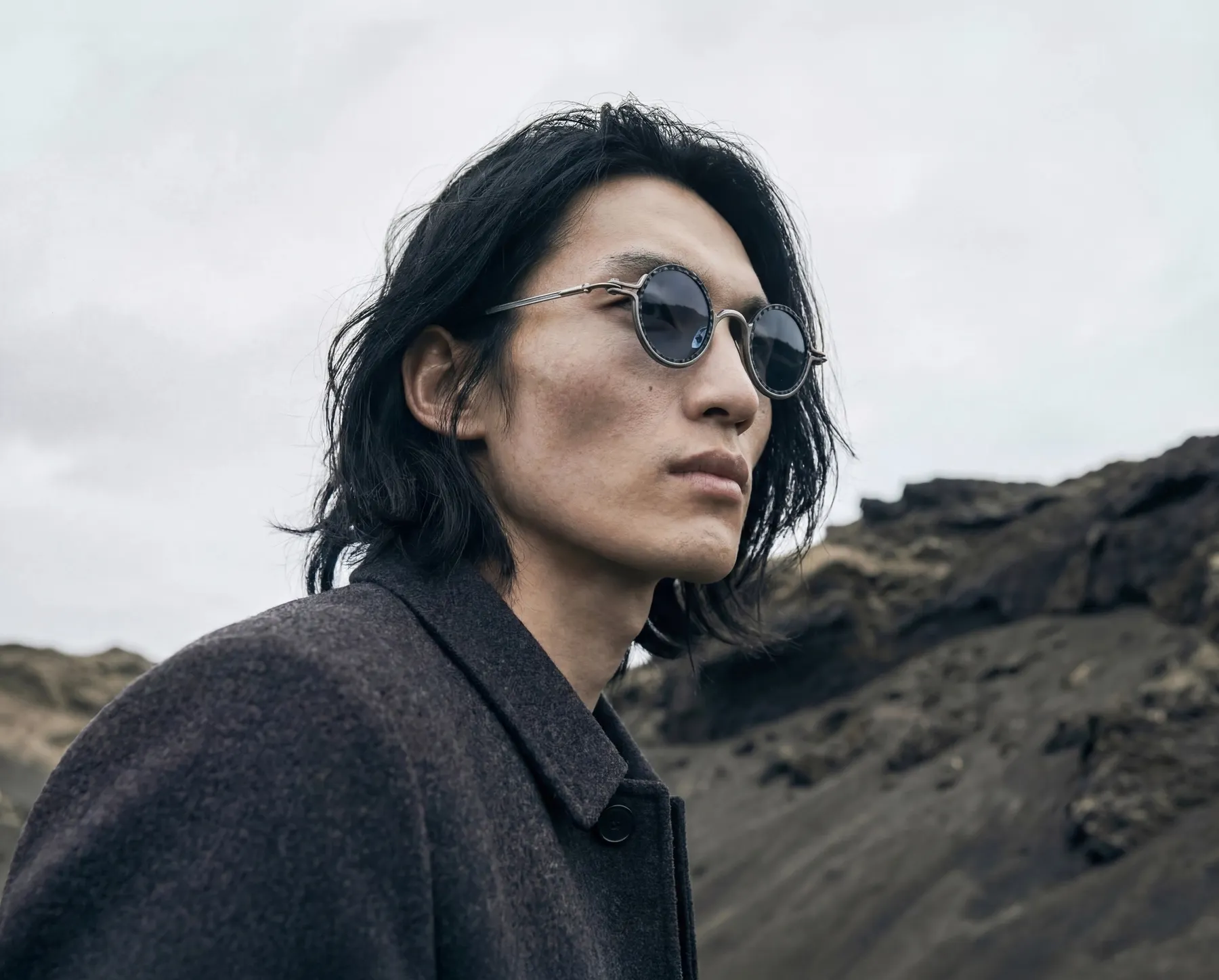 TAVAT campaign portrait wearing round sunglasses against a rocky landscape