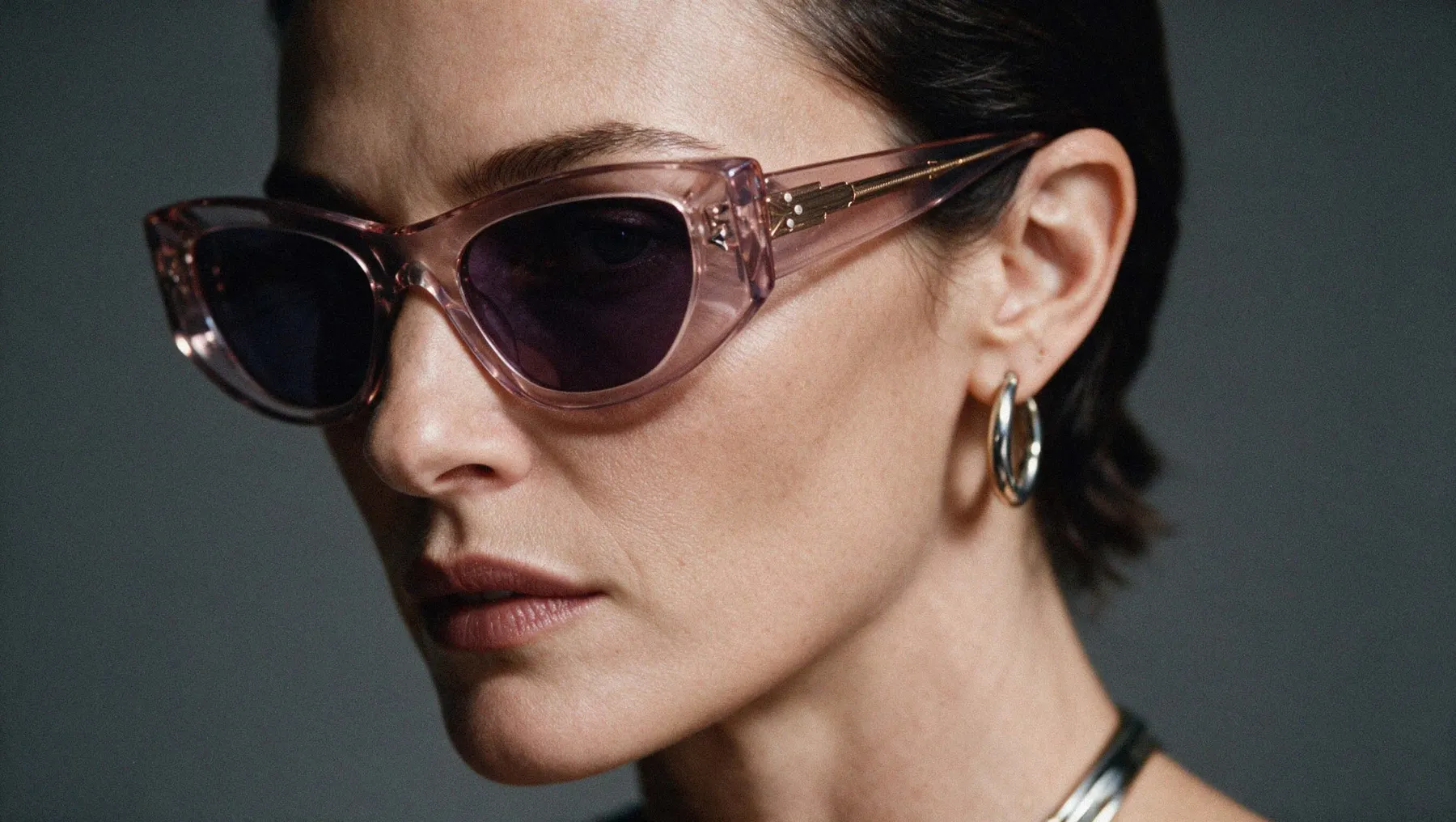 Woman wearing Pray Dina sunglasses, clear pink frame and grey lenses